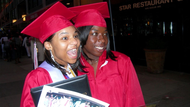 Two students wearing caps and gowns and smiling