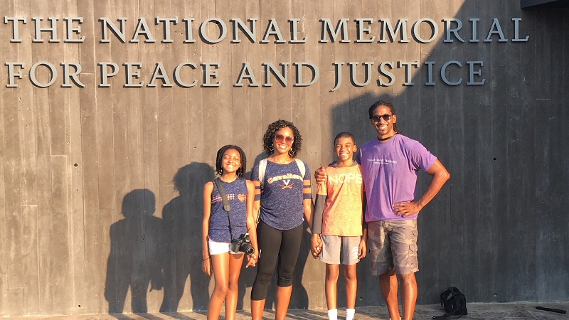 Author Nicole Tucker Smith with her husband and two children standing in front of a sign reading The National Monument for Peace and Justice.