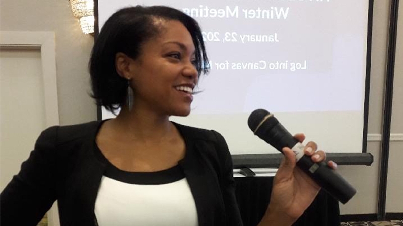 Nicole Tucker Smith smiling and holding a microphone while giving a presentation.